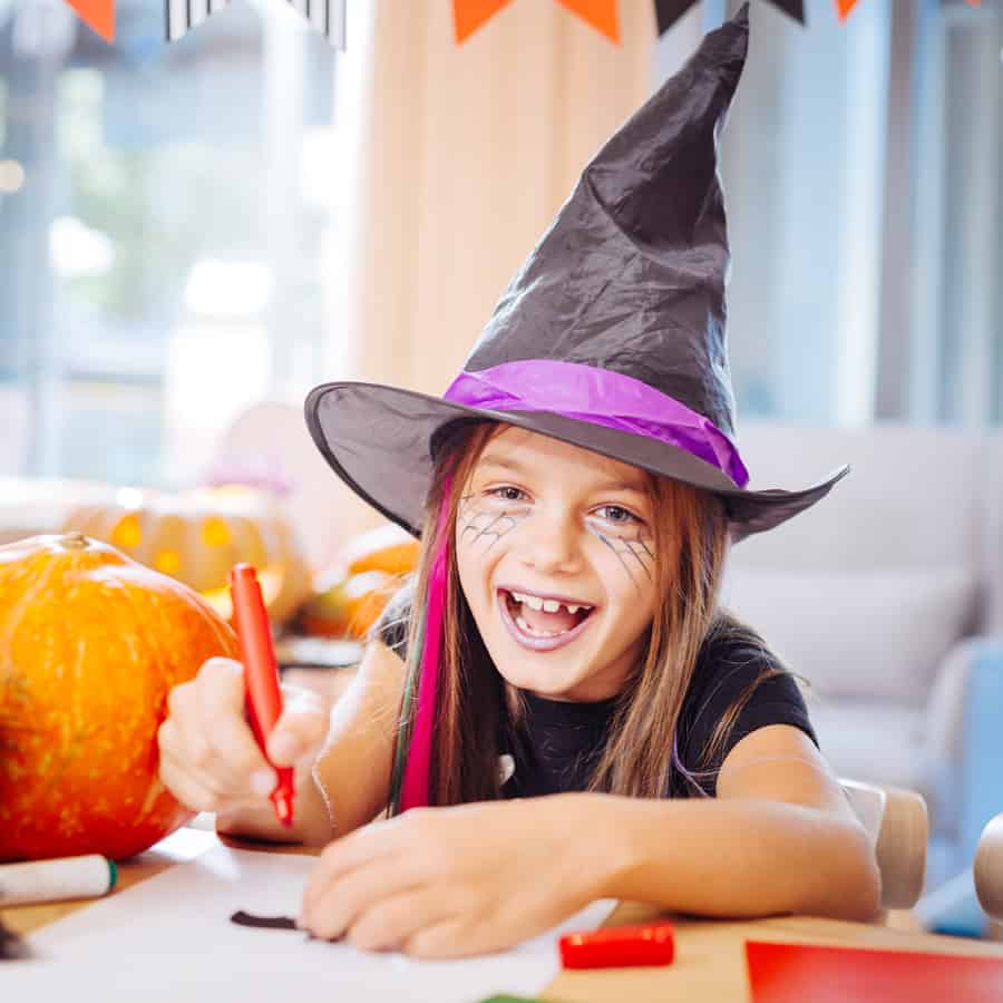 Laughing and drawing. Blue-eyed girl wearing wizard Halloween costume laughing while drawing scary pictures